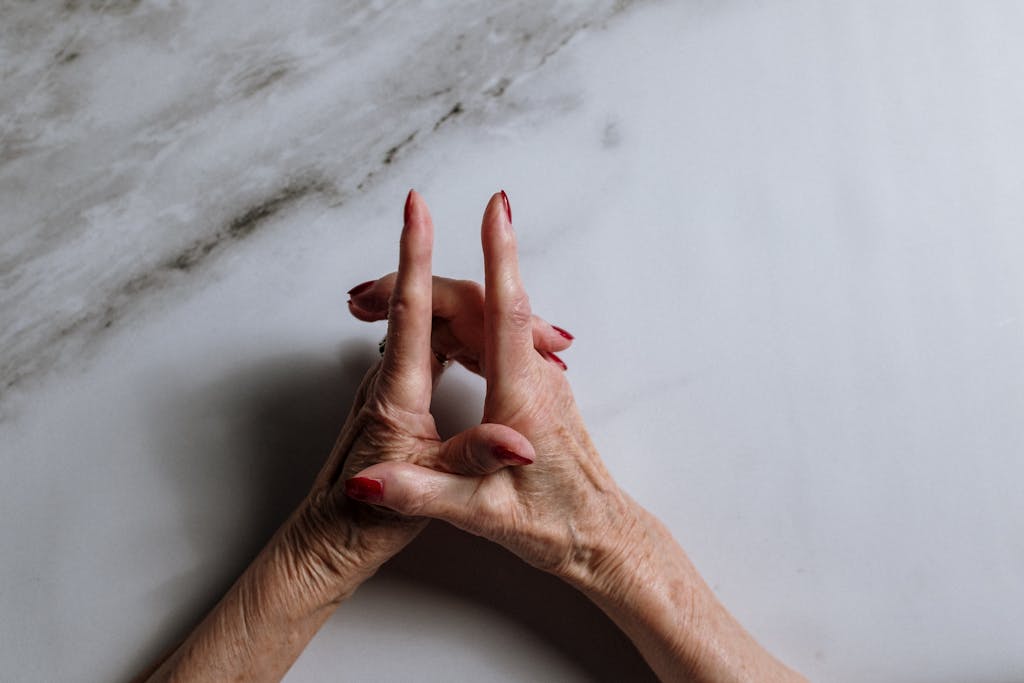 Close-up of an elderly woman's elegant hands with red nail polish on a marble background.